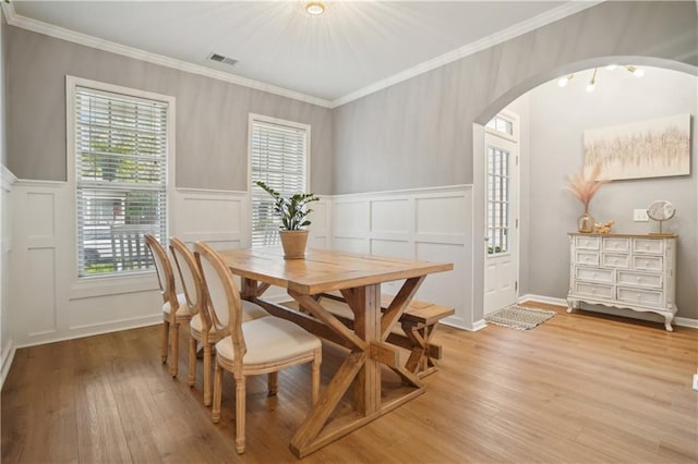 dining room with a decorative wall, arched walkways, light wood-type flooring, ornamental molding, and visible vents
