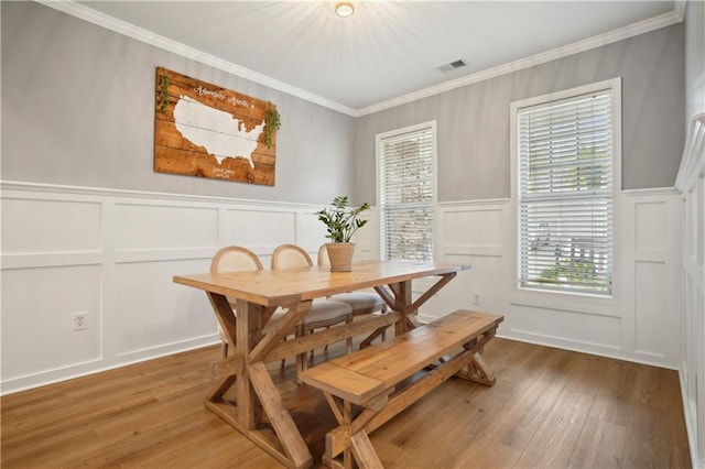 dining area with a decorative wall, visible vents, wood finished floors, and crown molding