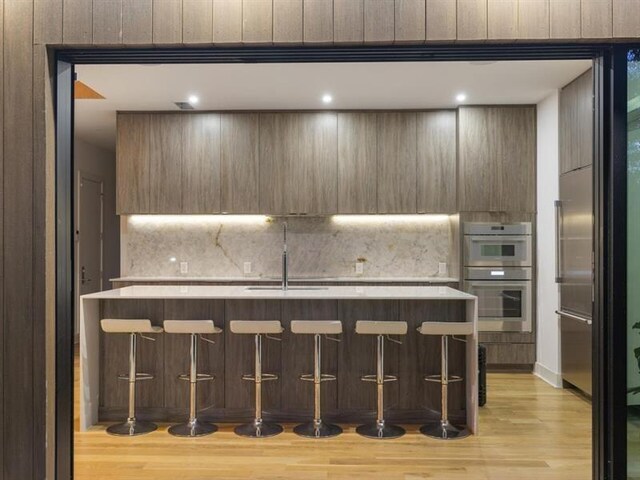 kitchen featuring sink, a breakfast bar area, stainless steel double oven, and light hardwood / wood-style flooring