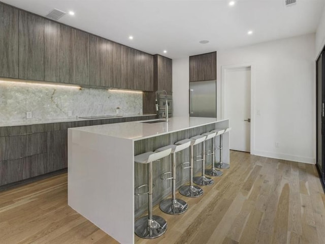 kitchen with sink, stainless steel built in fridge, light wood-type flooring, a breakfast bar area, and a center island with sink