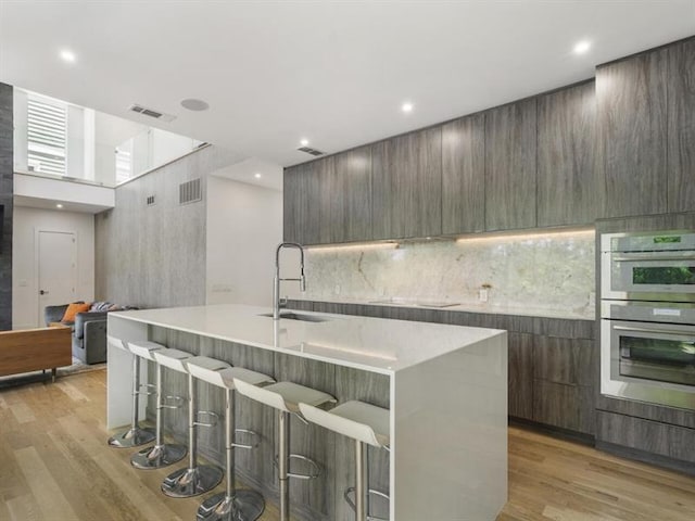 kitchen featuring sink, an island with sink, a breakfast bar area, and double oven