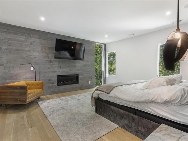 bedroom featuring a fireplace, light hardwood / wood-style flooring, and multiple windows