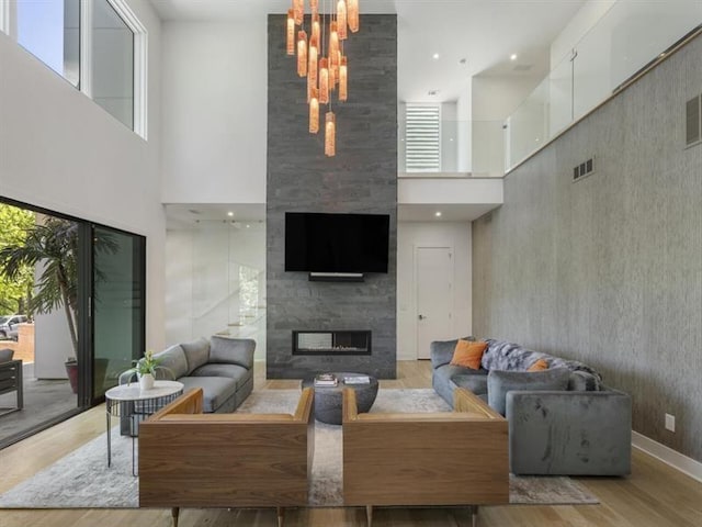 living room with a high ceiling, light wood-type flooring, and a tiled fireplace