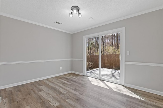 empty room featuring crown molding, visible vents, a textured ceiling, wood finished floors, and baseboards