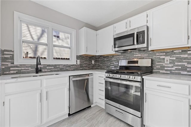 kitchen featuring light countertops, backsplash, appliances with stainless steel finishes, white cabinets, and a sink