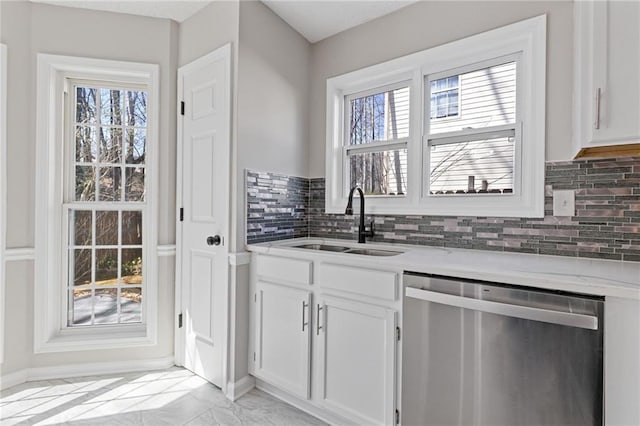 kitchen with tasteful backsplash, white cabinets, dishwasher, marble finish floor, and a sink