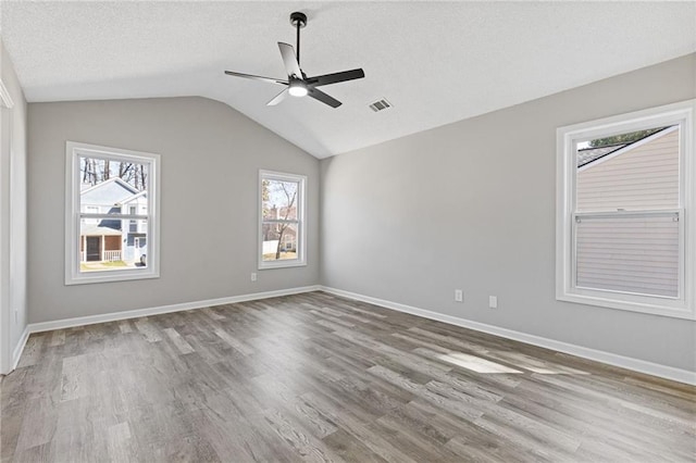 spare room with vaulted ceiling, wood finished floors, visible vents, and baseboards