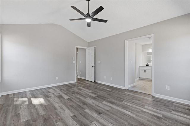 unfurnished bedroom featuring baseboards, ceiling fan, ensuite bath, wood finished floors, and vaulted ceiling