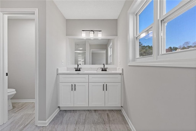 full bathroom with baseboards, a sink, toilet, and double vanity