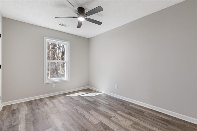 spare room with a ceiling fan, visible vents, baseboards, and wood finished floors