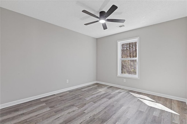 empty room featuring baseboards, a textured ceiling, visible vents, and wood finished floors