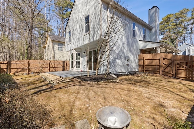 back of house featuring a chimney, a patio area, a fenced backyard, and a gate