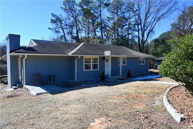 ranch-style house featuring roof with shingles, a patio, a chimney, and stucco siding