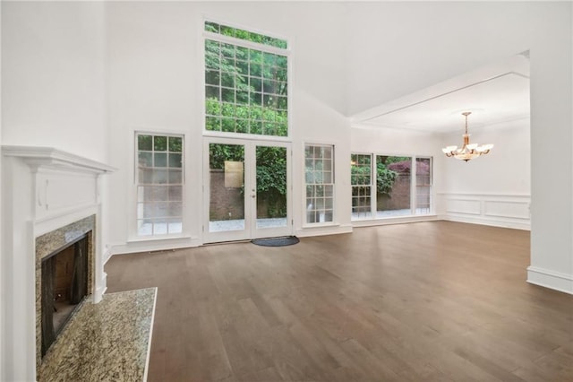 unfurnished living room with a notable chandelier, a fireplace, a wealth of natural light, and dark wood-type flooring