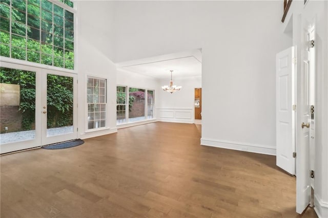 unfurnished living room with a high ceiling, a notable chandelier, and hardwood / wood-style floors