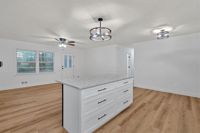 kitchen with white cabinetry, decorative light fixtures, light hardwood / wood-style floors, and light stone counters