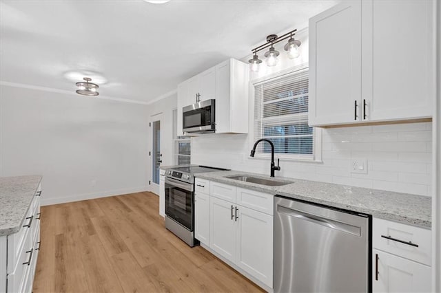 kitchen with appliances with stainless steel finishes, white cabinetry, sink, backsplash, and light stone countertops