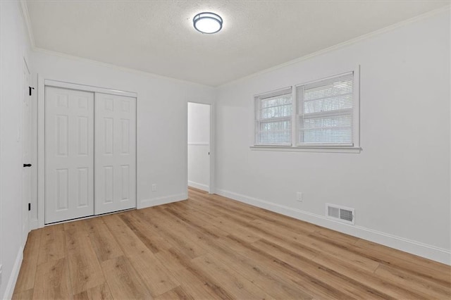 unfurnished bedroom featuring ornamental molding, a textured ceiling, a closet, and light wood-type flooring