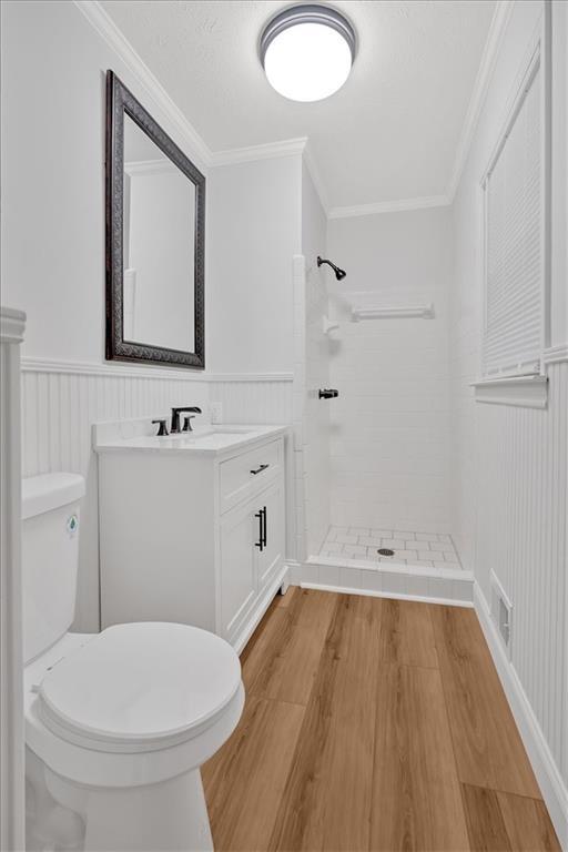 bathroom with hardwood / wood-style flooring, a tile shower, vanity, ornamental molding, and toilet