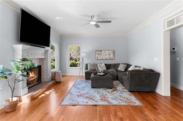 living area featuring ceiling fan, a tile fireplace, wood finished floors, baseboards, and ornamental molding