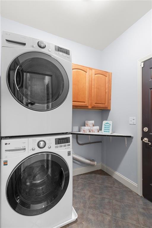 washroom featuring baseboards, cabinet space, and stacked washer / dryer