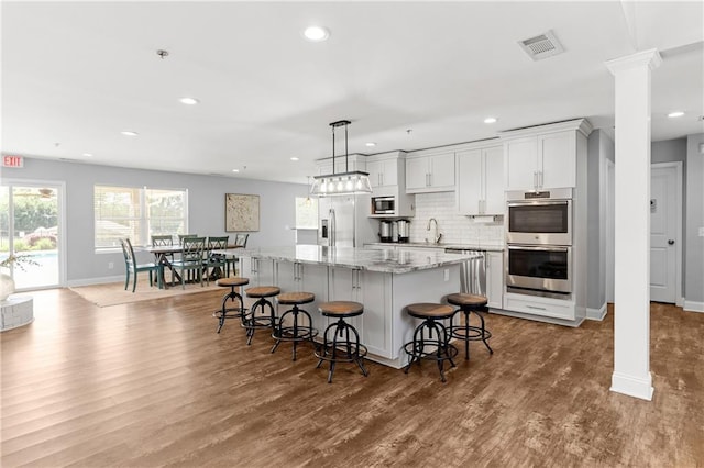 kitchen with appliances with stainless steel finishes, a center island, decorative columns, visible vents, and dark wood-style floors