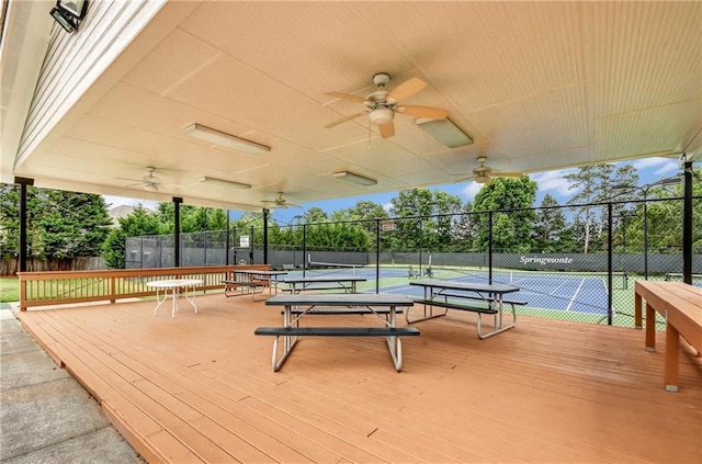 wooden terrace featuring ceiling fan, fence, and a tennis court