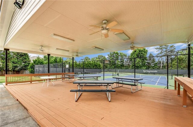 wooden terrace featuring ceiling fan, fence, and a tennis court