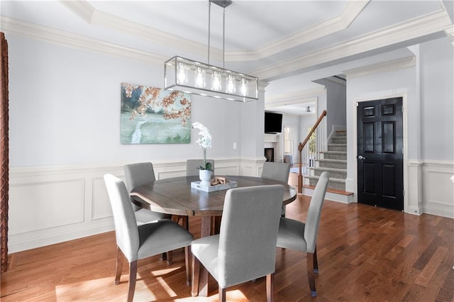 dining room featuring a tray ceiling, a fireplace, a decorative wall, and wood finished floors