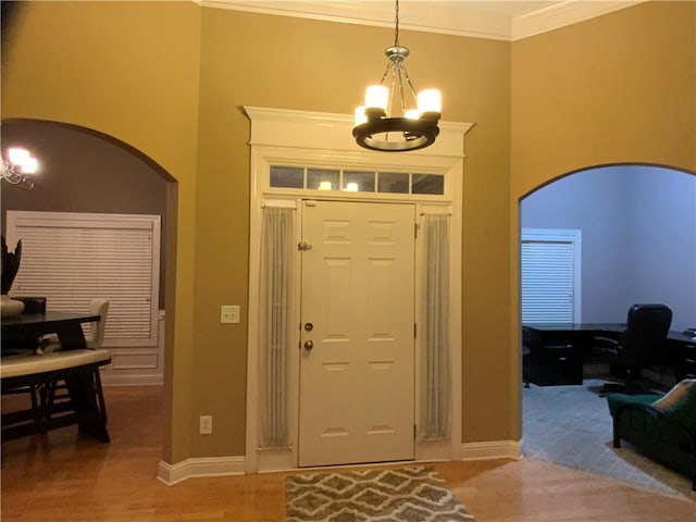 foyer with arched walkways, a towering ceiling, ornamental molding, wood finished floors, and a chandelier