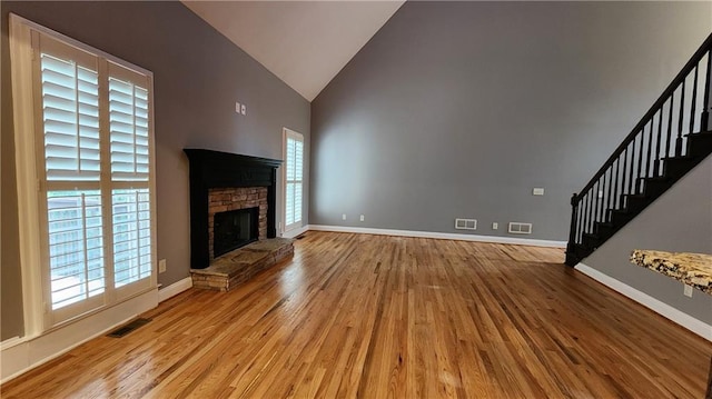 unfurnished living room with a wealth of natural light, a fireplace, high vaulted ceiling, and light hardwood / wood-style flooring