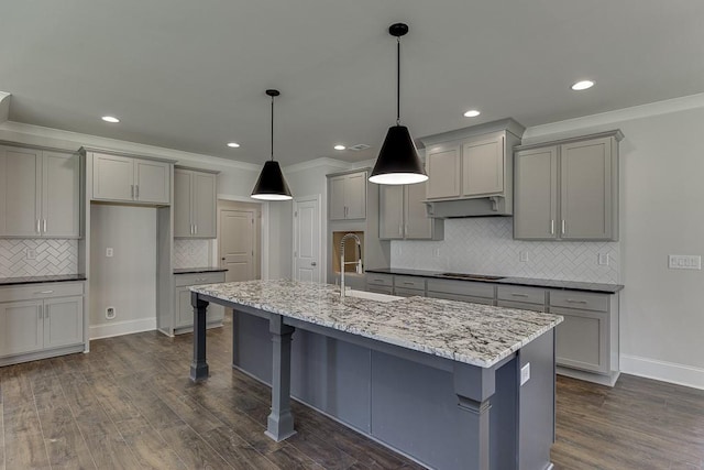 kitchen with light stone counters, decorative light fixtures, dark wood finished floors, gray cabinets, and an island with sink