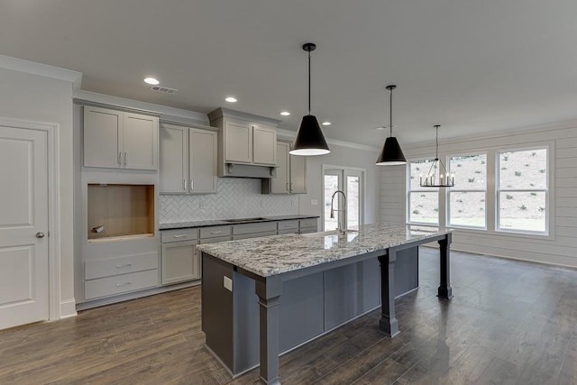 kitchen featuring light stone counters, decorative light fixtures, gray cabinetry, a kitchen island with sink, and a sink