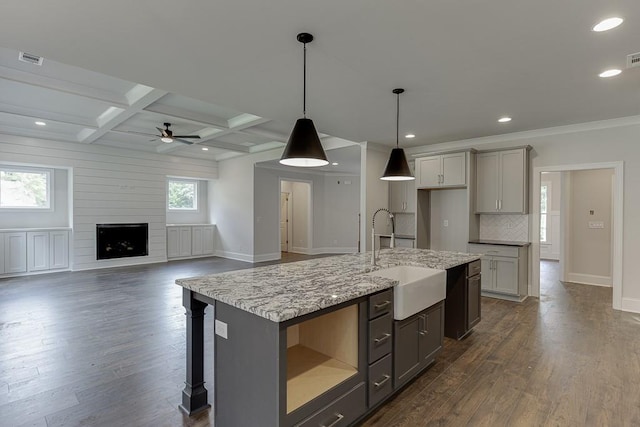 kitchen featuring decorative light fixtures, gray cabinets, open floor plan, a sink, and an island with sink