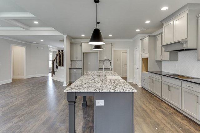 kitchen with black electric stovetop, gray cabinetry, a sink, a center island with sink, and pendant lighting