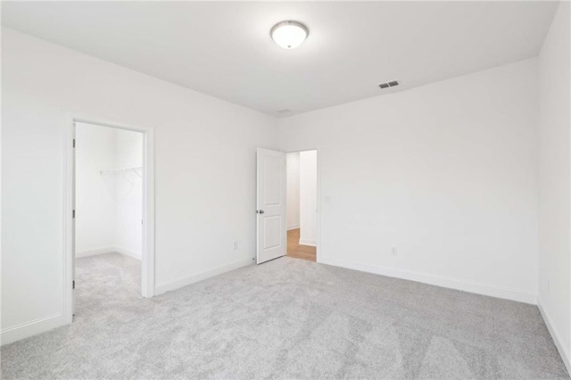 unfurnished bedroom with baseboards, visible vents, light colored carpet, a walk in closet, and a closet