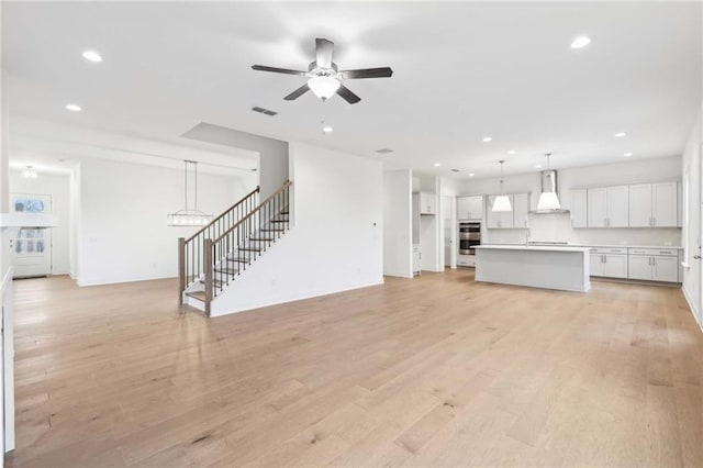 unfurnished living room with a ceiling fan, light wood-type flooring, recessed lighting, and stairs