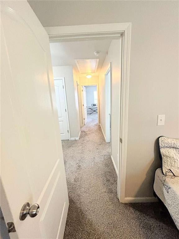 hallway featuring attic access, light colored carpet, and baseboards