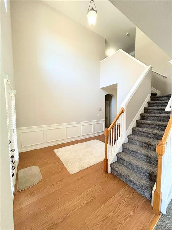 staircase with arched walkways, a wainscoted wall, a decorative wall, and wood finished floors