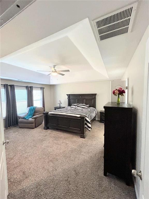 bedroom with a tray ceiling, visible vents, carpet, and ceiling fan