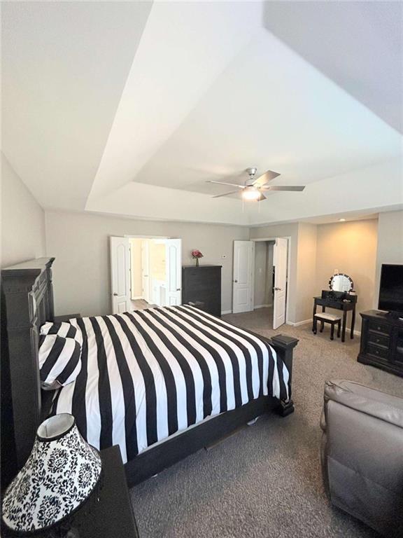 carpeted bedroom with a tray ceiling, a ceiling fan, and baseboards