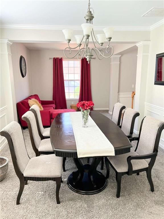 carpeted dining area featuring an inviting chandelier, ornate columns, and ornamental molding