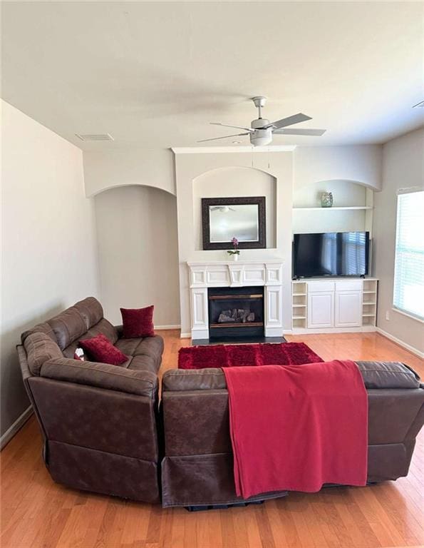 living area featuring a fireplace with flush hearth, baseboards, a ceiling fan, and wood finished floors