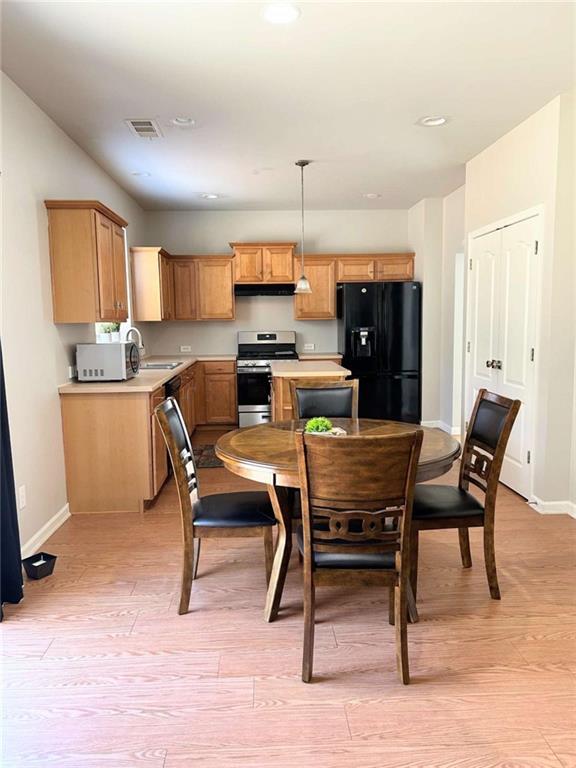 kitchen featuring visible vents, a sink, stainless steel range with electric stovetop, under cabinet range hood, and black fridge