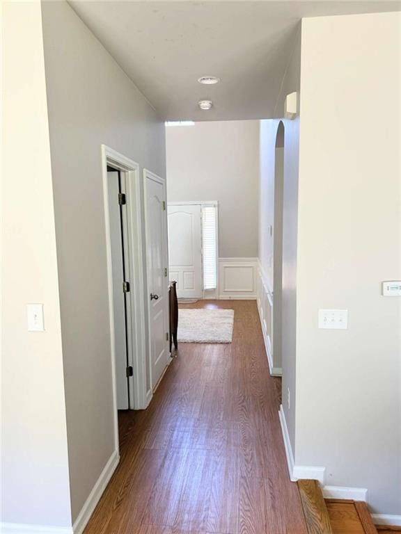 corridor with arched walkways, a decorative wall, dark wood-type flooring, and baseboards