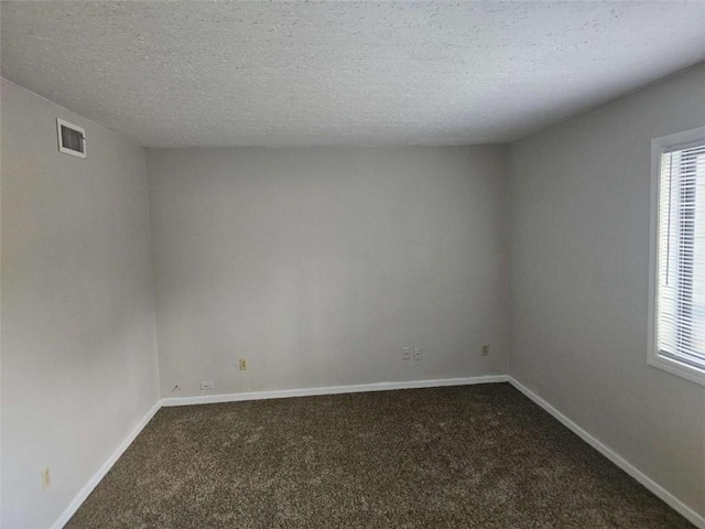 empty room featuring plenty of natural light, a textured ceiling, and dark carpet