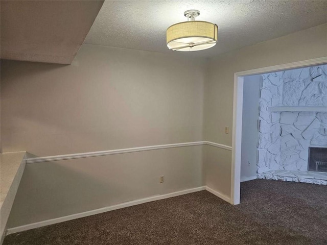 interior space with a stone fireplace, a textured ceiling, and dark colored carpet