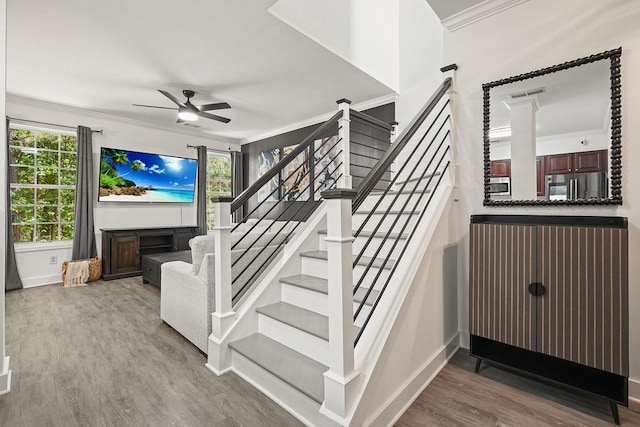 stairs with a fireplace, wood-type flooring, ornamental molding, and ceiling fan