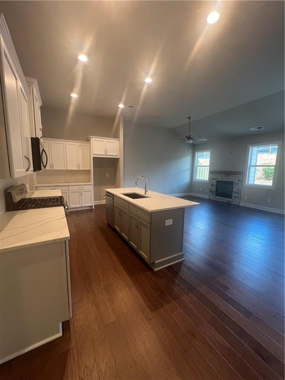 kitchen featuring a fireplace, sink, white cabinets, a kitchen island with sink, and range