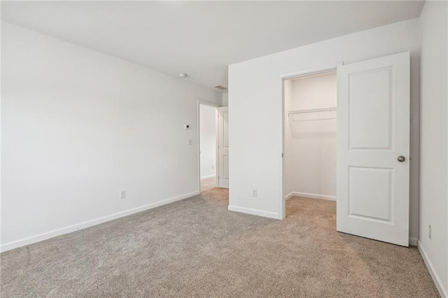 unfurnished bedroom featuring a spacious closet, light carpet, and a closet